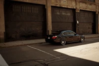 Black BMW M5 E60 parked on a city street, showcasing its sleek design and alloy wheels against an industrial backdrop.