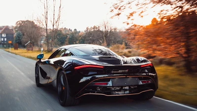 McLaren Senna negro en movimiento en una carretera escénica rodeada de árboles de otoño.