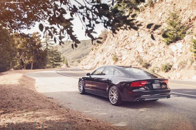 Audi A7 navegando em uma estrada montanhosa sinuosa, exibindo seu design elegante e rodas de liga esportivas.