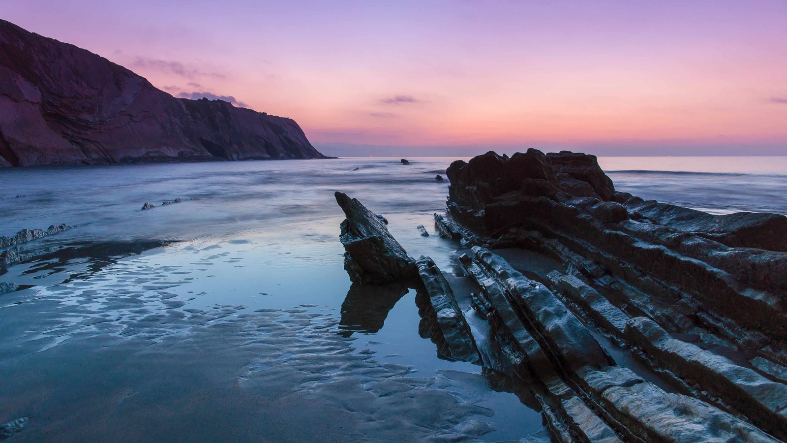 Arafed rock formation on the beach at sunset with a pink sky (sea, ocean, coast, headland, shore)