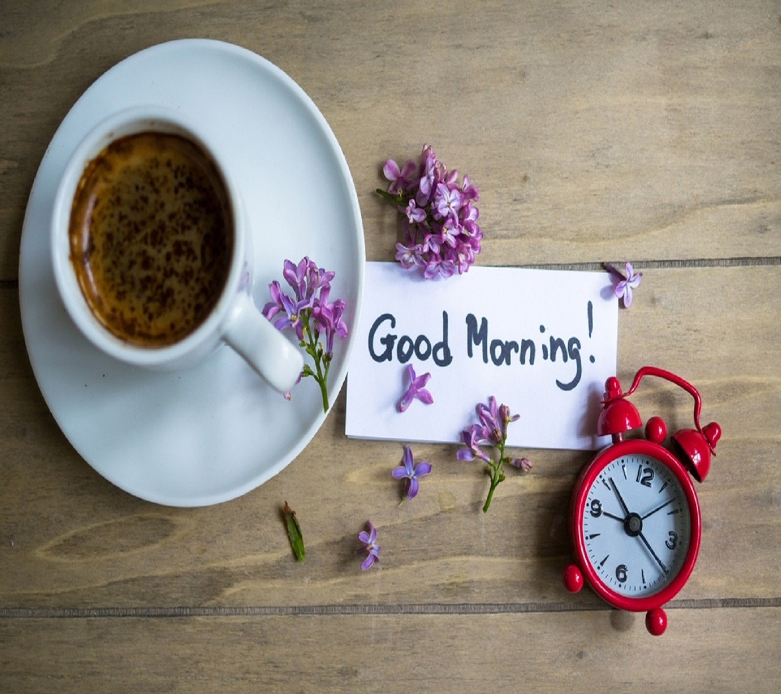 Una taza de café y un pequeño reloj despertador rojo (buen, mañana)