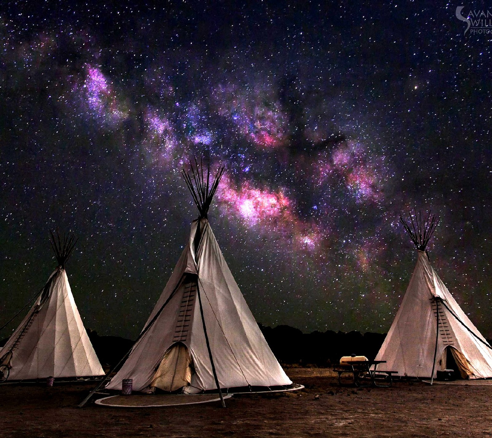 Trois tipis se trouvent dans un champ sous un ciel étoilé (nuit)