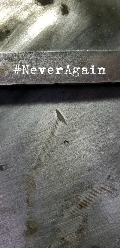 #NeverAgain: A scratched metal surface with a bold inscription.