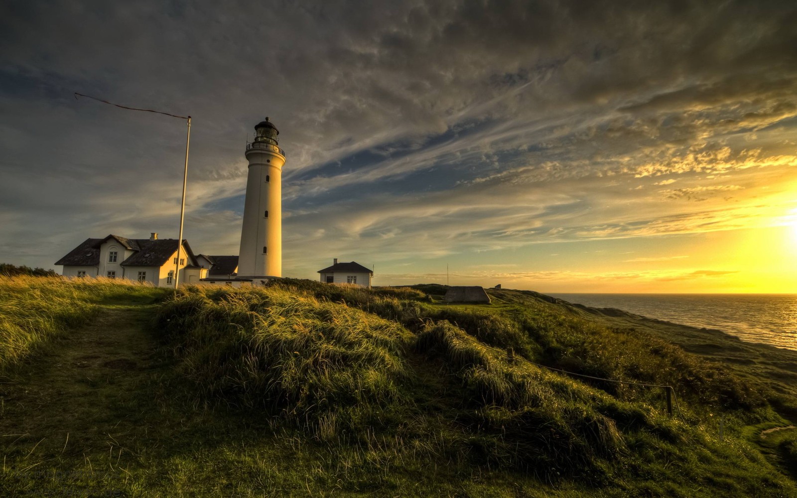 Un primer plano de un faro en una colina cubierta de hierba cerca del océano (faro, torre, nube, costa, noche)