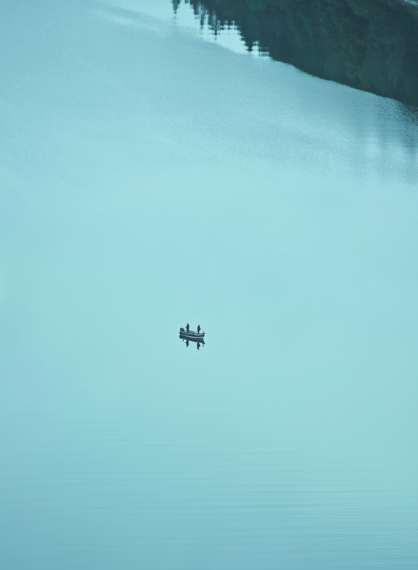 There is a small boat floating in the middle of a lake (blue, green, turquoise, aqua, azure)