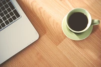 Tasse de café à côté d'un ordinateur portable sur un bureau en bois