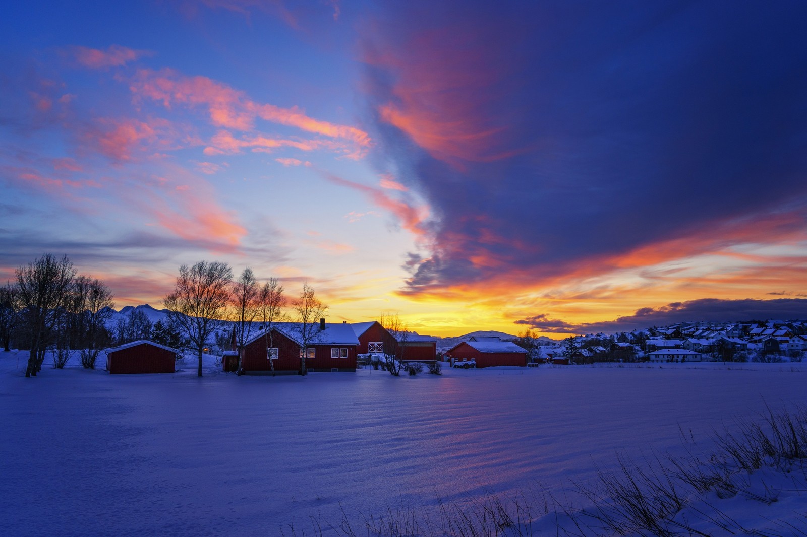 Une vue d'un coucher de soleil sur un champ enneigé avec quelques maisons (coucher de soleil, lever de soleil, nuage, hiver, crépuscule)