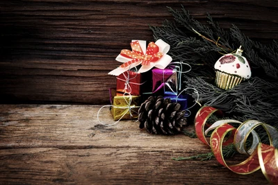 Colorful Christmas gifts and a decorative cupcake are arranged with pinecones and festive ribbons against a rustic wooden background.