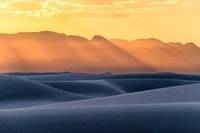 A luz dourada banha as dunas onduladas do Monumento Nacional White Sands, com montanhas distantes silhuetadas contra um vibrante céu matutino.