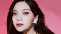 Umji de VIVIZ irradia encanto contra un vibrante fondo rosa, mostrando sus cautivadoras características y brillantes accesorios.