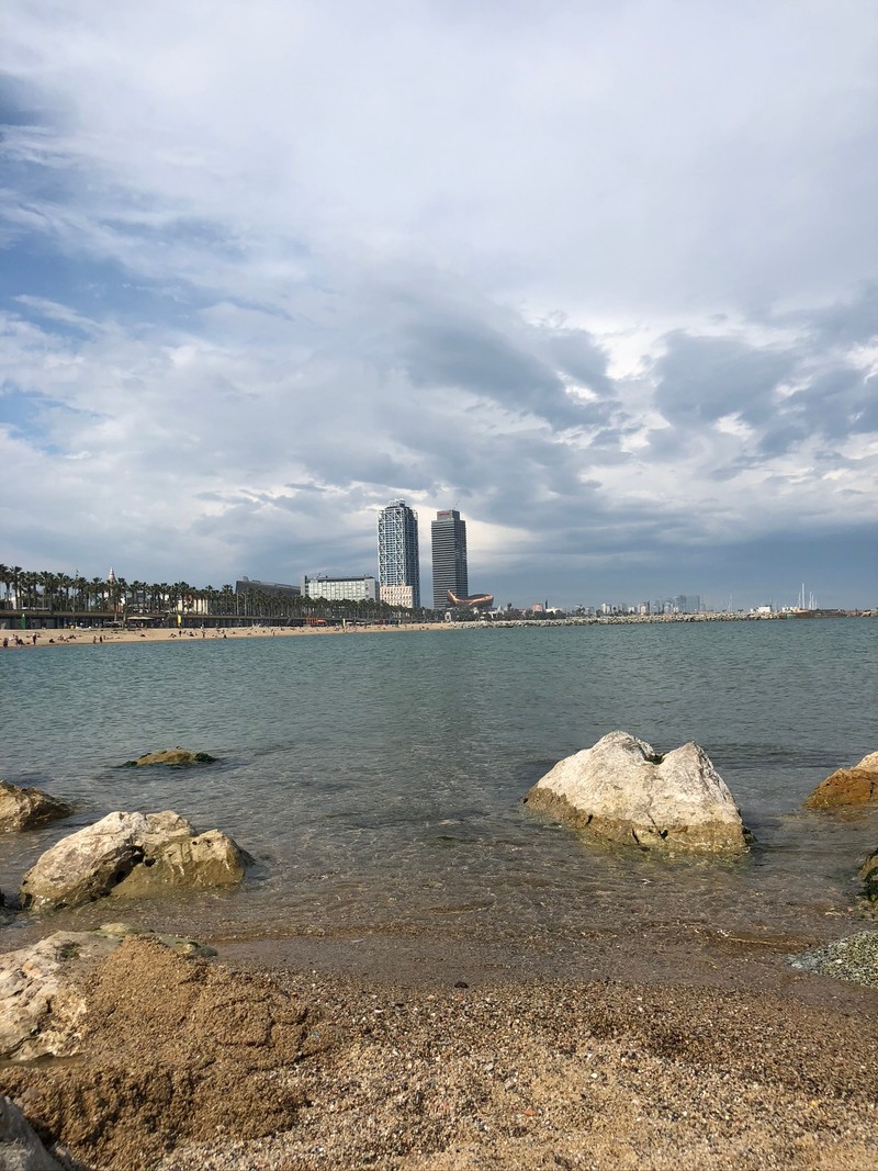 Вид на пляж с камнями и зданием на фоне (море, водоем, облако, побережье, жидкость)