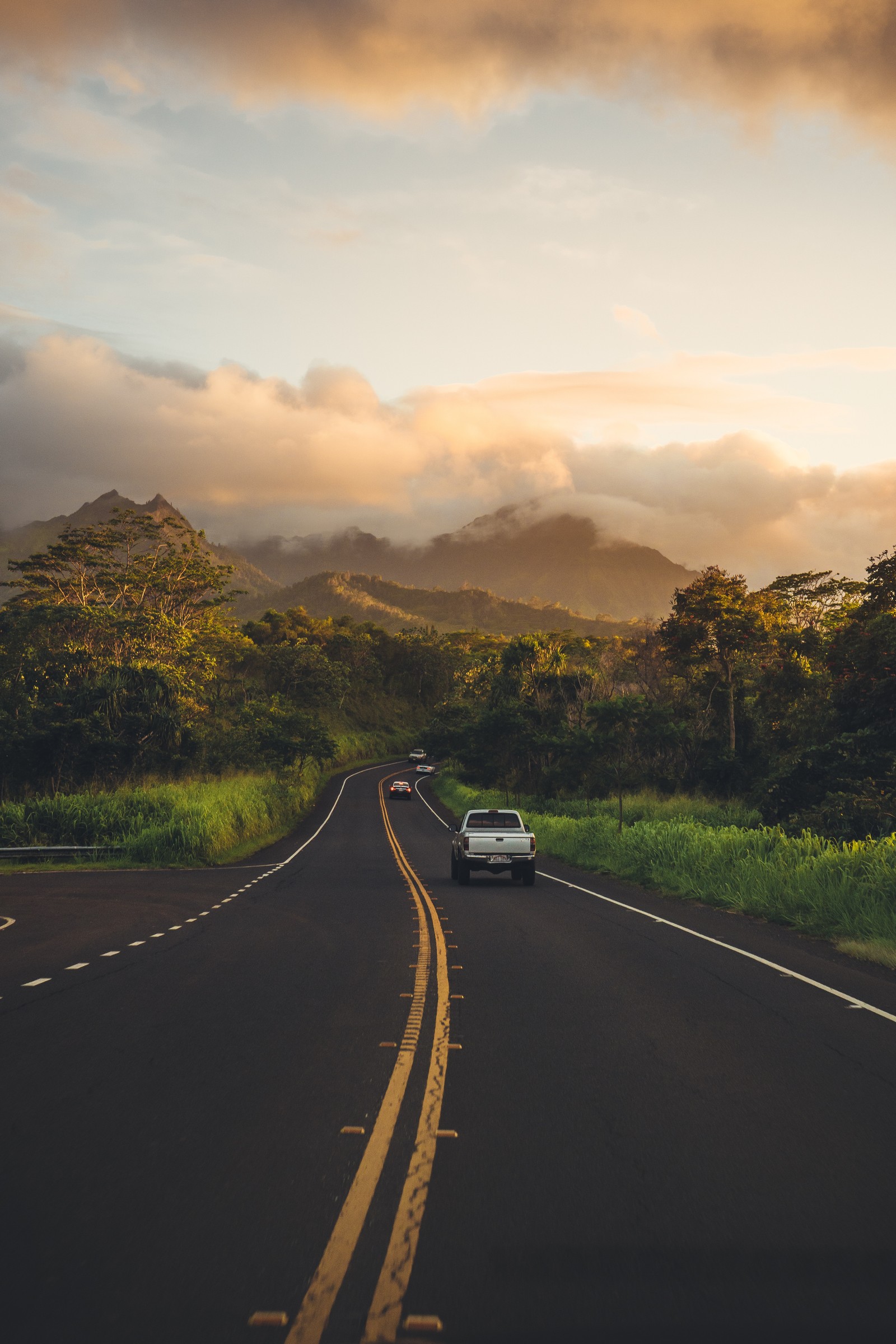 Vista panorámica de un coche conduciendo por una carretera con montañas al fondo (kauai, nube, planta, coches, montaña)