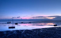 Pôr do sol sereno na praia com reflexos e veleiros