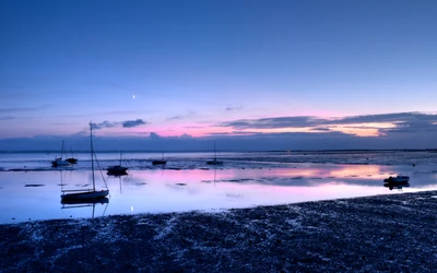 Atardecer sereno en la playa con reflejos y veleros