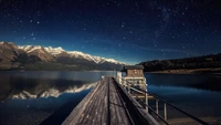 Noite estrelada sobre a paisagem montanhosa da Nova Zelândia e o píer sereno