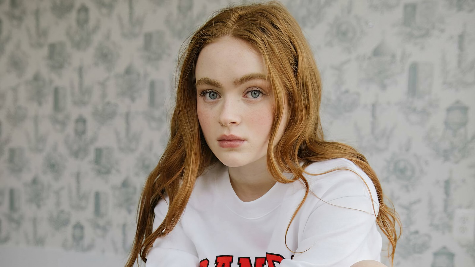 Une femme aux longs cheveux rouges assise sur un lit (sadie sink, américain, actrice, célébrité, filles)