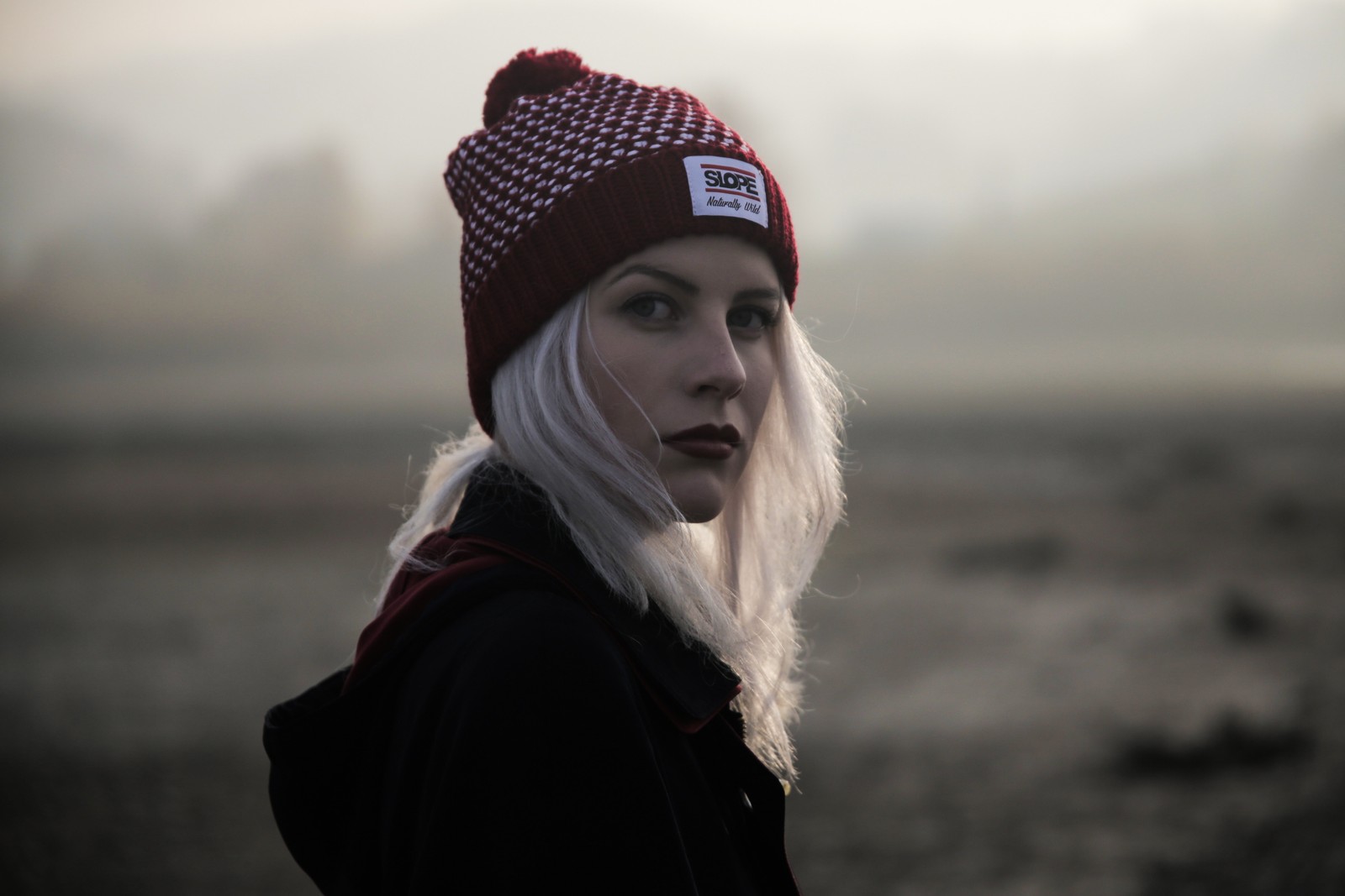 Una mujer rubia con cabello blanco que lleva un sombrero rojo y un abrigo negro (sombrero, moda, ropa de abrigo, ojo, nube)