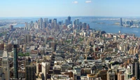 Ein Panoramablick auf die Skyline von New York City, der hohe Wolkenkratzer und die städtische Landschaft von Manhattan unter einem klaren blauen Himmel zeigt.