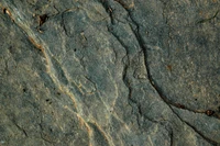 Textured Igneous Rock Outcrop with Soil and Grass Highlights