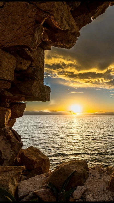 Vista do pôr do sol através de um arco rochoso sobre um mar calmo