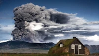 Vulcão em erupção se erguendo sobre uma paisagem montanhosa com uma cabana islandesa tradicional em primeiro plano.