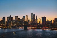 El horizonte de Manhattan al atardecer, mostrando el paisaje urbano iluminado y el puente de Manhattan sobre el río Este.