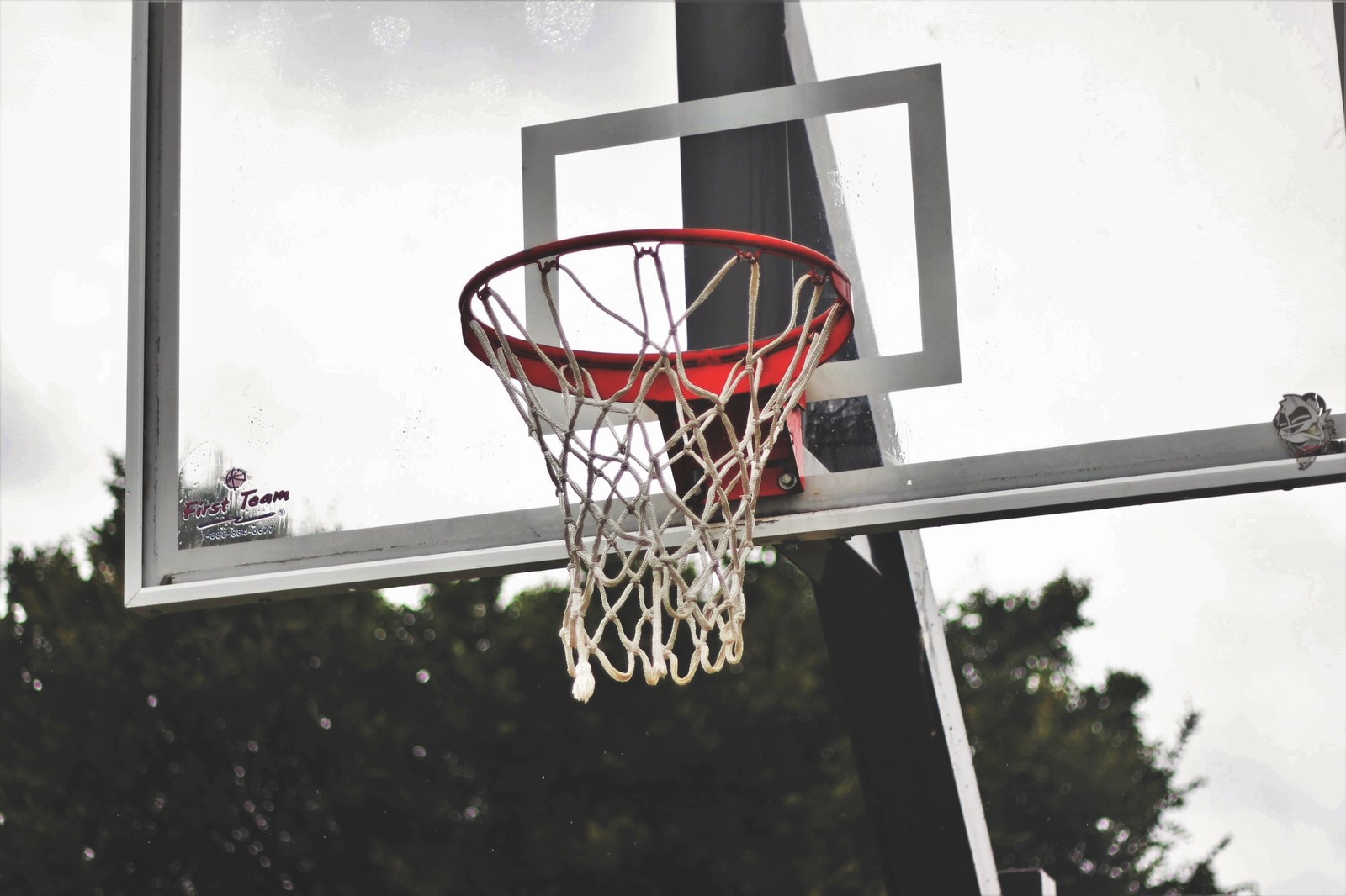 There is a basketball hoop with a net and a ball in it (basketball, backboard, basketball court, team sport, streetball)