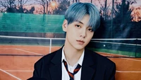 Soobin de TXT posa con un atuendo elegante frente a un fondo de cancha de tenis, reflejando una mezcla de encanto juvenil y estilo artístico.