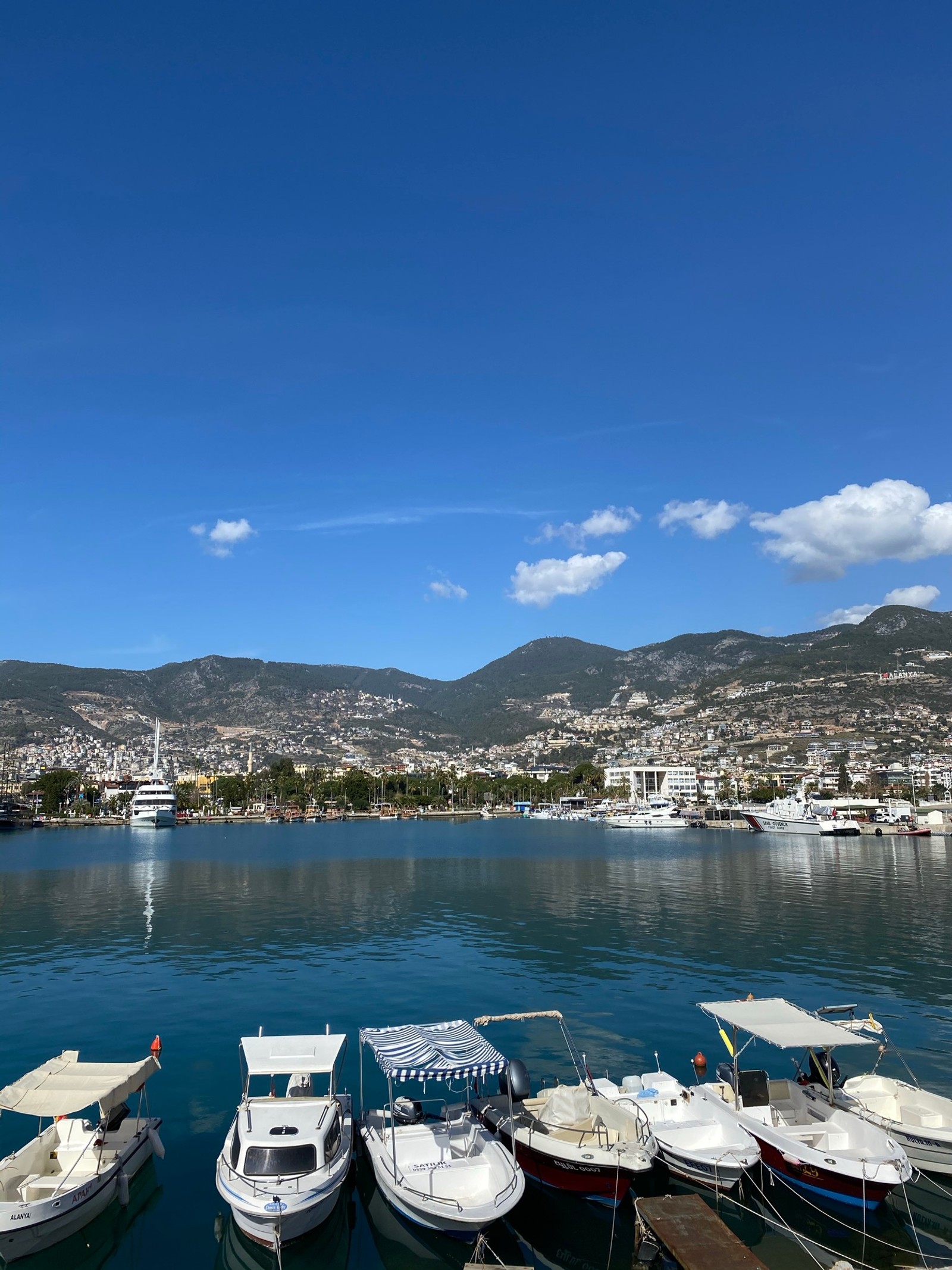 Los barcos están atracados en el agua cerca de una ciudad en un día soleado (yate, agua, nube, barco, montaña)