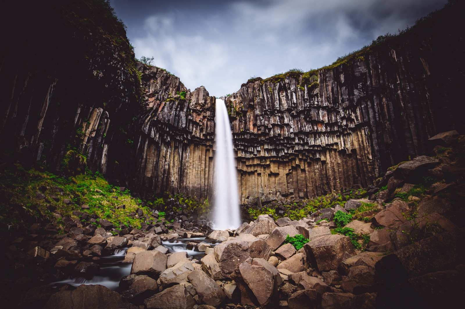 Uma cachoeira no meio de uma área rochosa com pedras e árvores (cachoeira svartifoss, islândia, parque nacional de vatnajökull, colunas de lava, rochas)