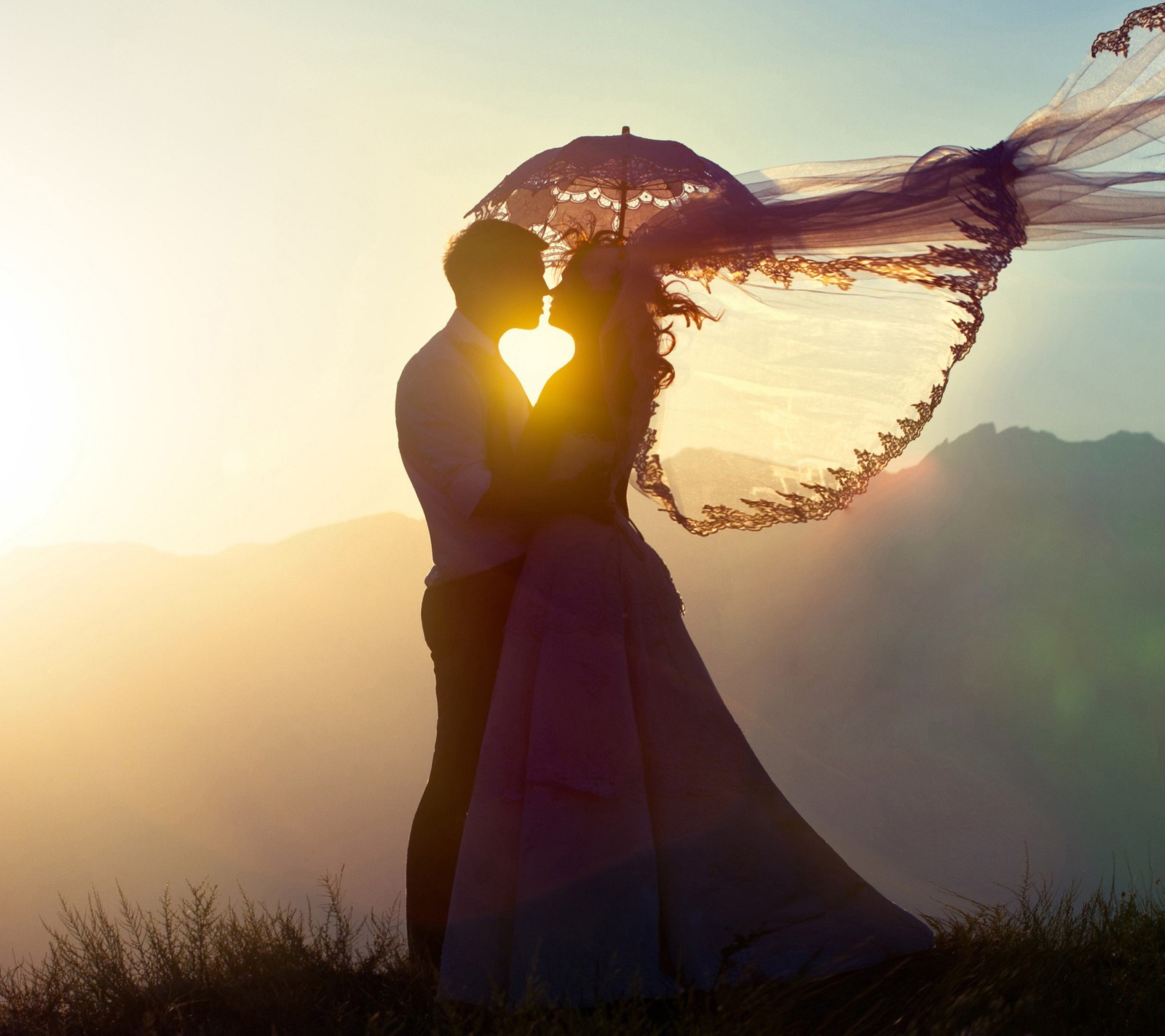 La mariée et le marié s'embrassent dans les montagnes au coucher du soleil avec un voile flottant au vent (amour, naturel, coucher de soleil)