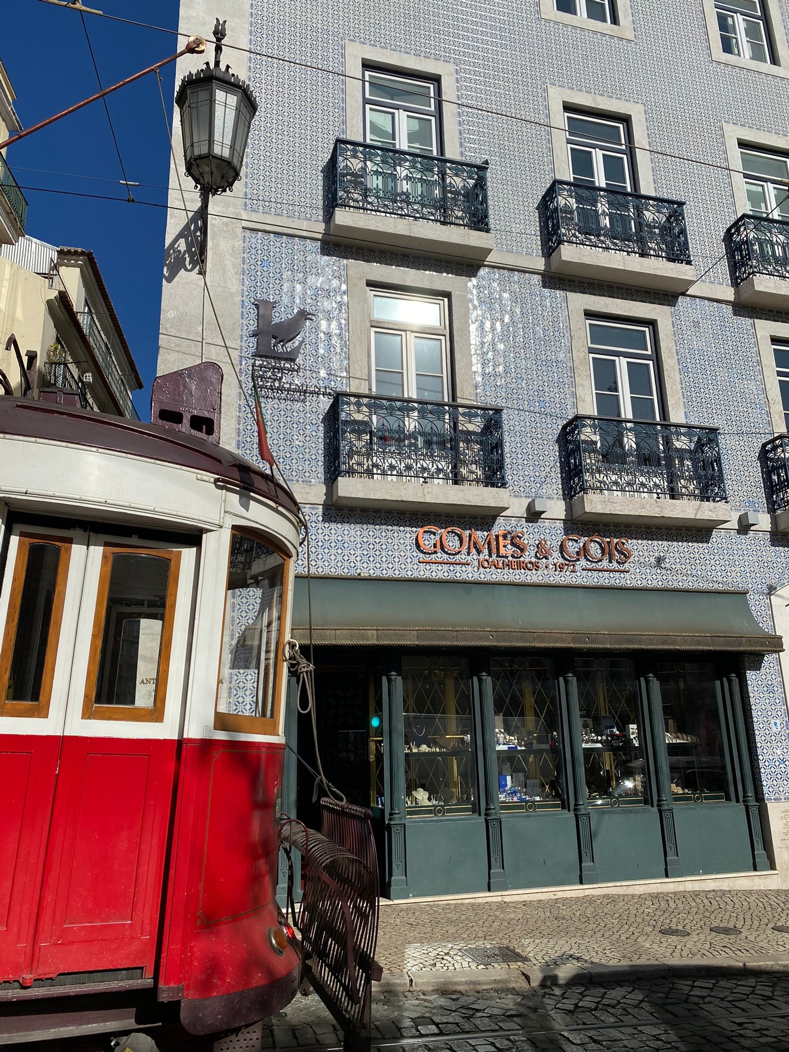 Vue aérienne d'un tramway dans une rue devant un bâtiment avec un panneau indiquant "gomes" (téléphérique, fenêtre, façade, électricité, alimentation électrique)