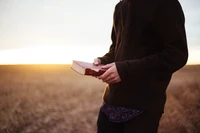 La luz del sol de la mañana ilumina una mano que sostiene un texto religioso en un paisaje sereno