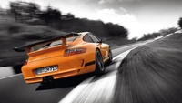 Porsche 911 GT3 RS 996 in auffälligem Orange, dynamisch auf einer kurvenreichen Straße mit einem dramatischen Schwarz-Weiß-Hintergrund navigierend.