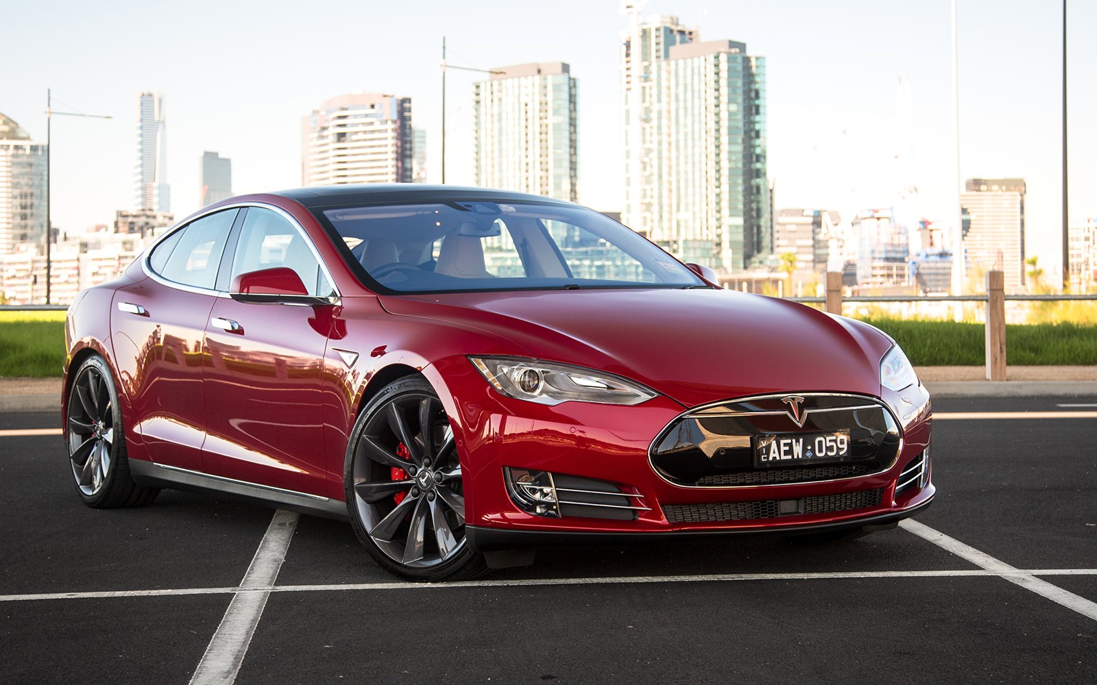 Un tesla model s rojo estacionado en un estacionamiento con una ciudad de fondo (coche, tesla model s, llanta, tesla model x, coche mediano)