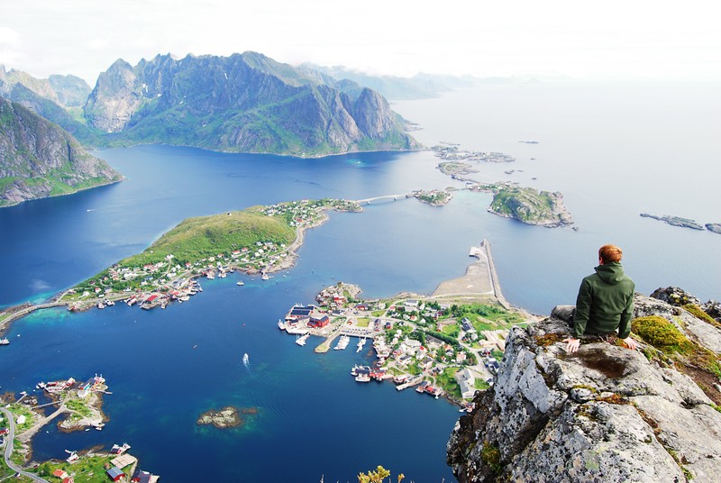 Арабский человек сидит на камне с видом на большое водоем (лофотены, lofoten, фьорд, мыс, вход)