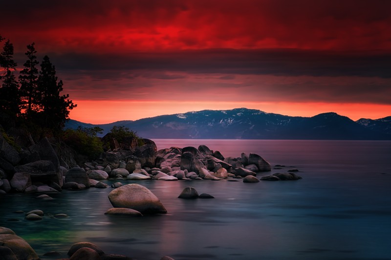 Вид на озеро с камнями и деревьями на переднем плане (озеро тахо, sand harbor, сумерки, длительная выдержка, закат)