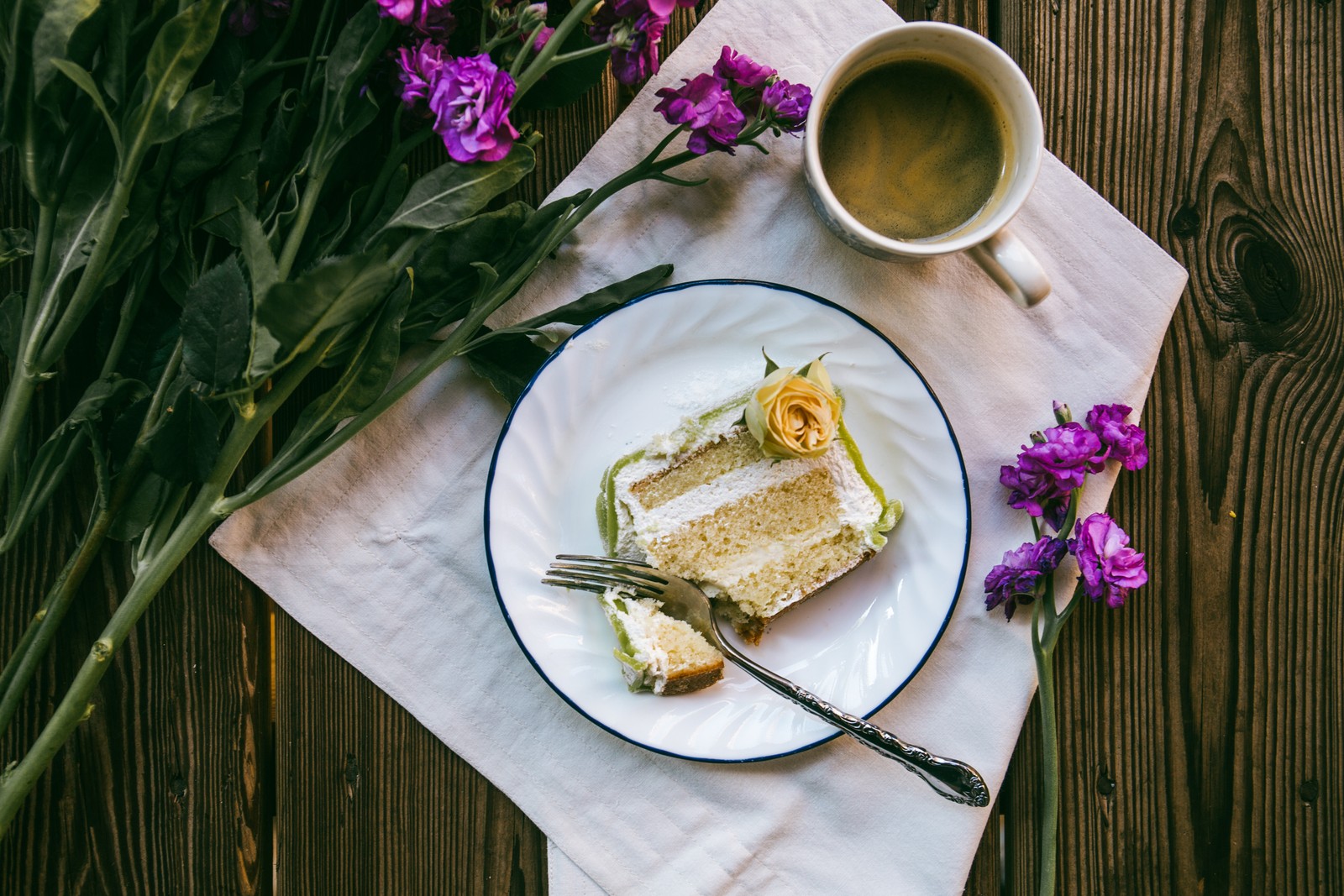 Hay un trozo de pastel en un plato con un tenedor y una taza de café (café, pastel, flor, taza de café, comida)