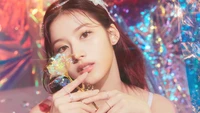 Sana von TWICE hält eine funkelnde Rose und strahlt Eleganz und Charme vor einem lebendigen, bunten Hintergrund aus.