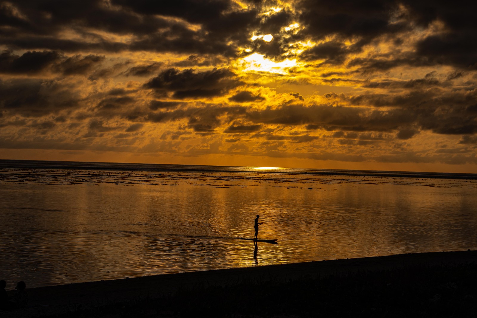 Un surfeur dans l'océan au coucher du soleil avec un ciel nuageux. (nuage, eau, ressources en eau, atmosphère, écorégion)