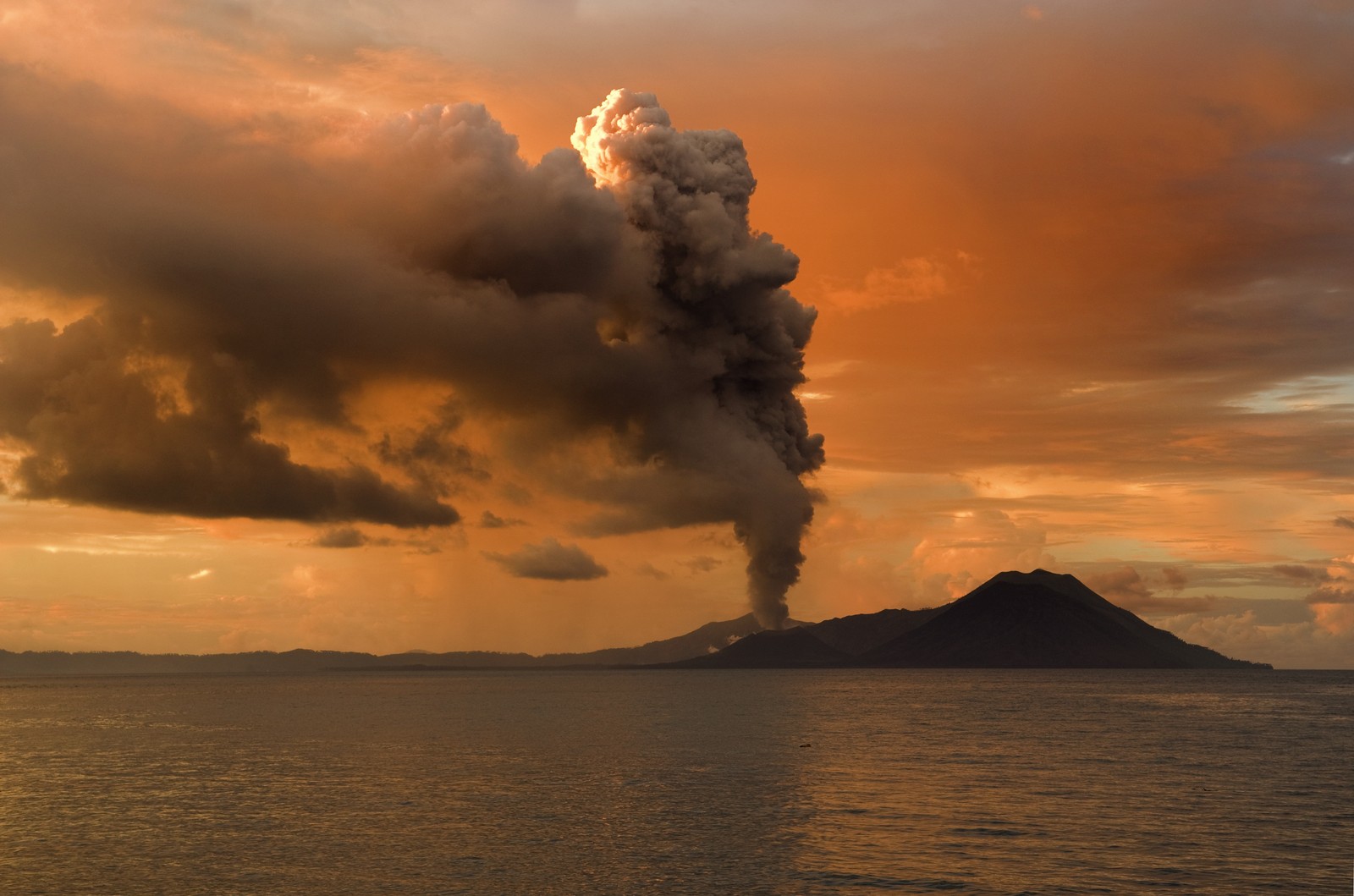 Vista aérea de un volcán arrojando humo al cielo sobre el océano (volcán, estratovolcán, nube, horizonte, mar)