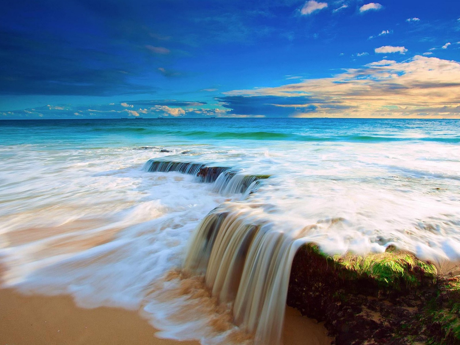 Una vista de una playa con una cascada saliendo del agua (hermoso, paisaje, naturaleza)