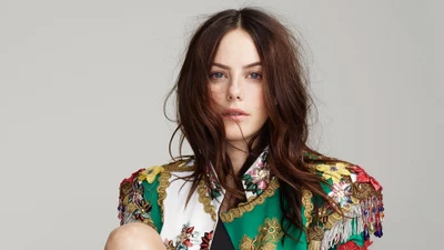 Kaya Scodelario in einem lebhaften, kunstvoll gestalteten Outfit, das ihre markanten Züge und braunen Haare zur Geltung bringt.