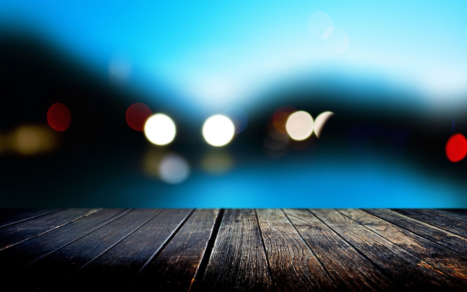 Eine nahaufnahme eines holztisches mit verschwommenen lichtern im hintergrund (blau, licht, wasser, tageszeit, macro)