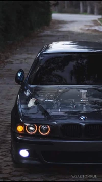 Élégant BMW E39 avec un affichage de moteur personnalisé sur le capot, garé sur un chemin serein bordé d'arbres.