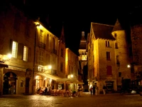 Charmanter mittelalterlicher Platz, der nachts beleuchtet ist und historische Architektur sowie einladendes Essen im Freien in einer lebhaften Hauptstadt zeigt.