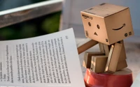 Robot Danbo leyendo al lado de un libro