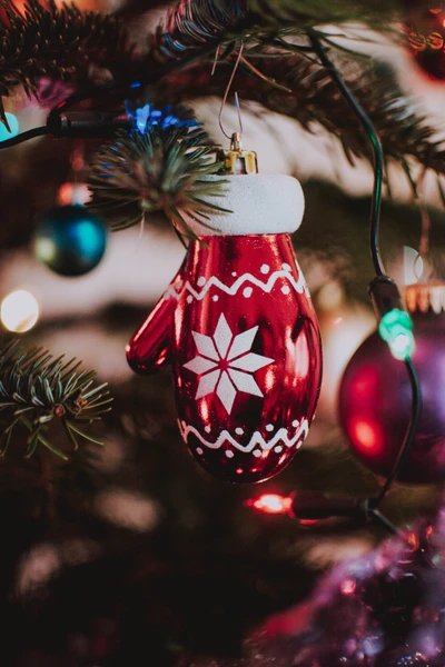 Rote Handschuh-Ornament, das an einem geschmückten Weihnachtsbaum mit bunten Lichtern hängt.