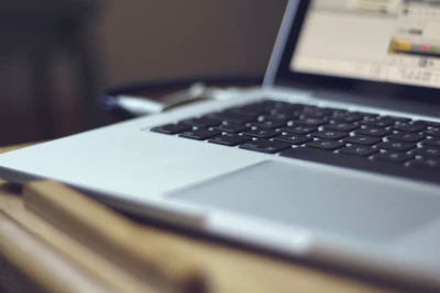 Close-up of a sleek MacBook keyboard on a desk with a blurred screen, symbolizing modern technology and productivity.