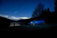 Coche deportivo compacto azul junto a un lago sereno bajo un cielo estrellado